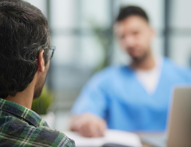 doctor in blue scrubs explains patient confidentiality to a man in a green plaid shirt